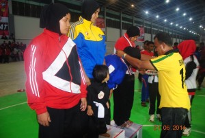 Kadispora Aceh Tengah Amir Hamzah mengalungkan medali kepada pemenang. Terlihat peraih emas Dewi dan anaknya di atas podium, disisi kirinya atlet Aceh Tengah Elda Singkite yang meraih medali perak.
